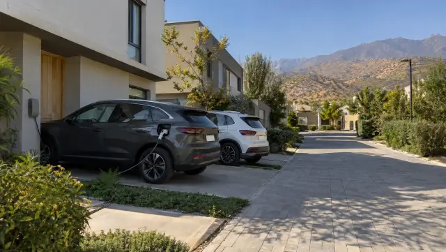 Pasaje de condominio de casas con un auto cargando en el muro lateral y la cordillera al fondo