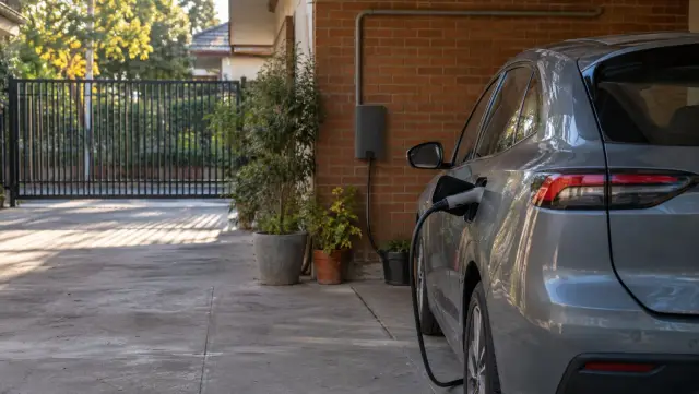 Auto eléctrico conectado a un cargador de pared en el garaje de una casa de ladrillo